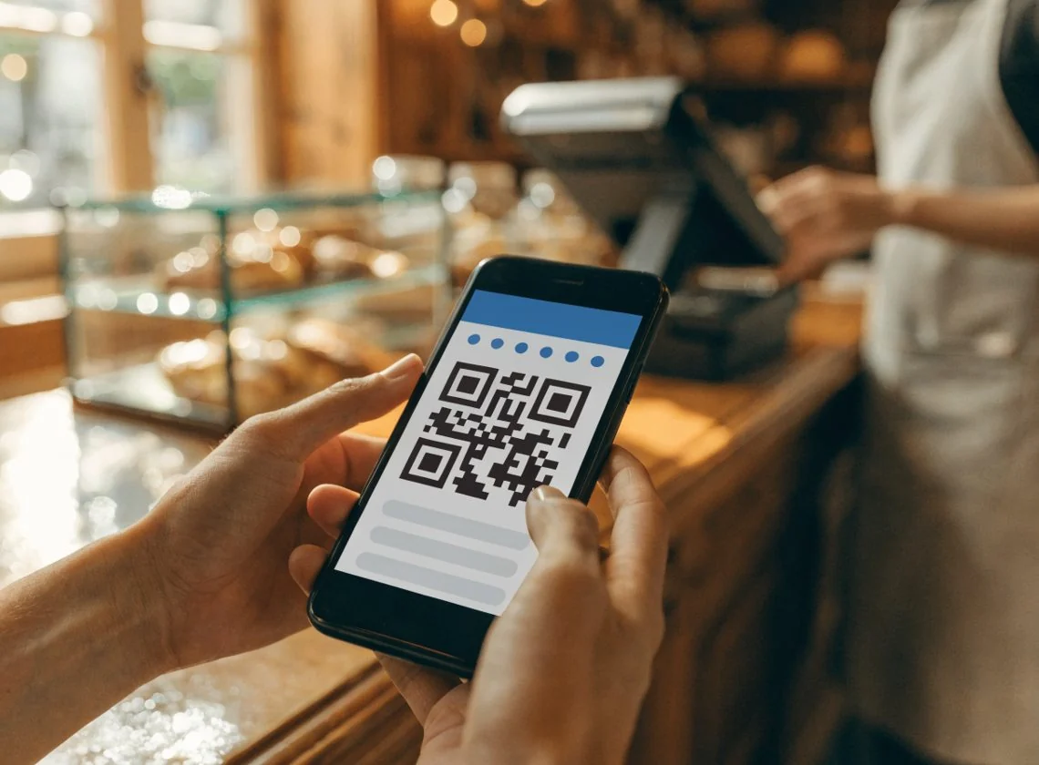 Un client présente sur son smartphone une carte de fidélité digitale avec QR code, au comptoir d’un café.