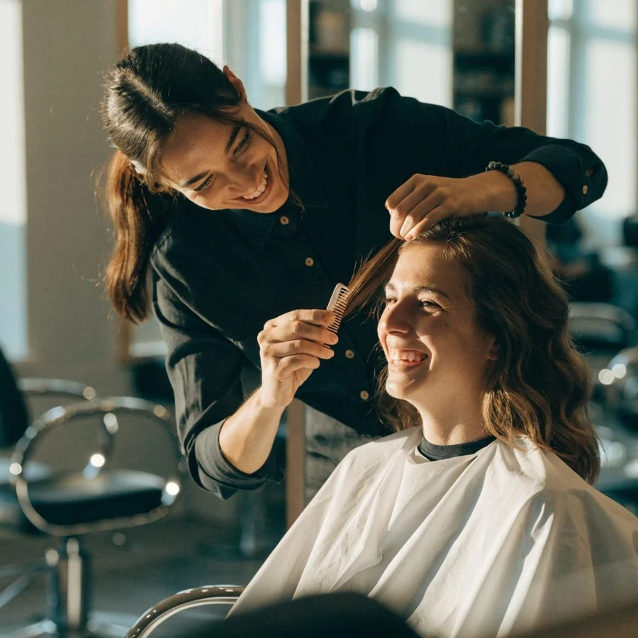 Une coiffeuse coiffe une cliente souriante dans un salon lumineux.